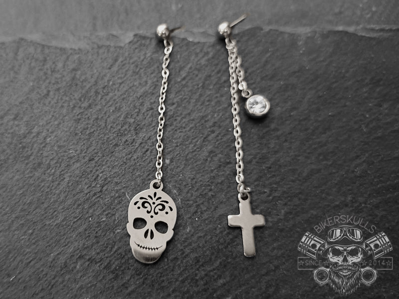 Orecchini asimmetrici con catenina in acciaio e ciondoli dal design gotici, teschio con piccola croce e punto luce in acciaio.