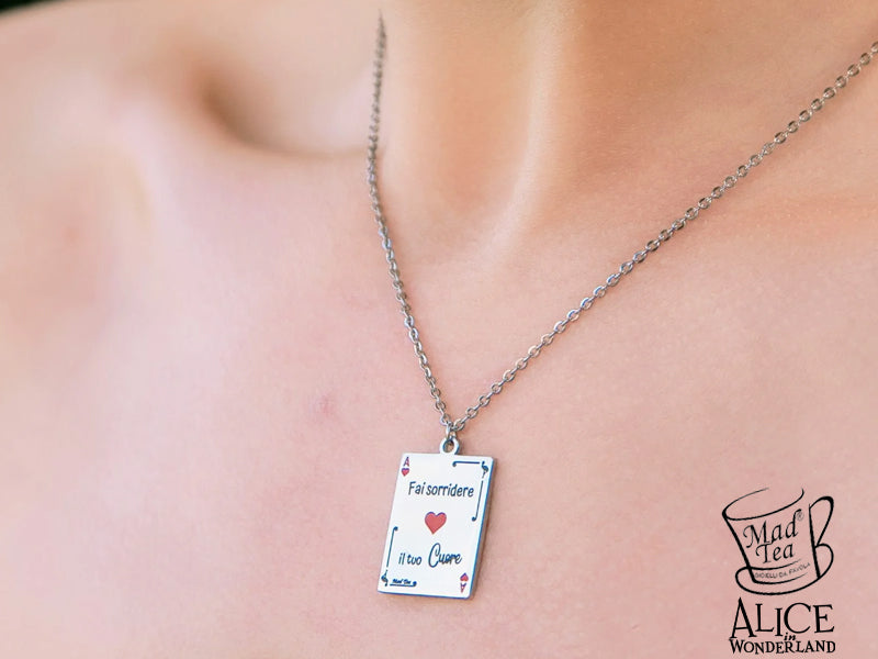 Collana con carta da gioco di Alice double face. Sul fronte è incisa la frase “Fai sorridere il tuo cuore” con un cuore rosso al centro e piccoli fenicotteri laterali mentre sul retro è incisa la frase “Solo allora troverai il Paese delle meraviglie” con un cuore dove all’interno c’è la serratura per Wonderland.

