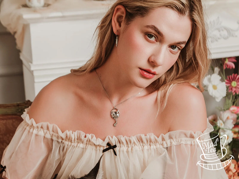 La collana Mad Tea è composta da due ciondoli in acciaio inossidabile 316L, un materiale anallergico e resistente. Il primo ciondolo raffigura lo Stregatto con l'incisione "Siamo tutti matti", mentre il secondo è una replica stilizzata della sua codina. La collana è disponibile in diverse lunghezze e rappresenta un accessorio unico e di alta qualità.