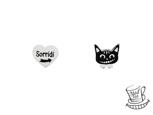 Orecchini a lobo asimmetrici con un piccolo cuore con la scritta “Sorridi” e la freccia che indica la direzione della felicità in uno e il muso del Gatto del Cheshire nell’altro. 