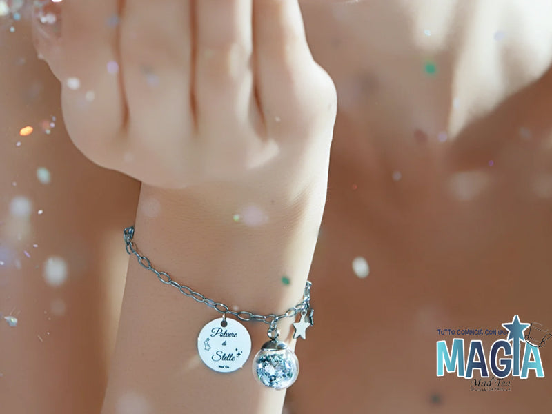 Bracciale in acciaio con sfera in vetro antiurto contenente piccole stelle di magia e targhetta con incisa la frase “Polvere di stelle”.