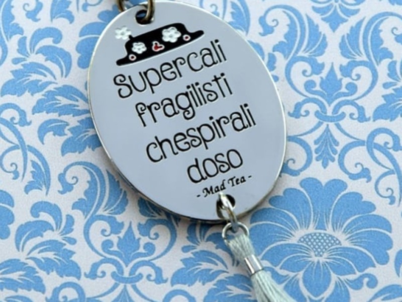 Collana con ciondolo composto da targhetta con incisa la frase "Supercalifragilistichespiralidoso" e il cappello di Mary Poppins e delicata nappina pendente. Catena a rosario in acciaio con cristalli.