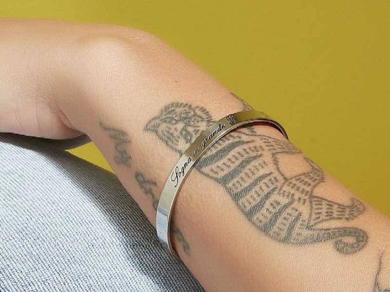 Ragazza tatuata con bracciale bangle rigido in acciaio con scritto sogna in grande e casetta di up con palloncini