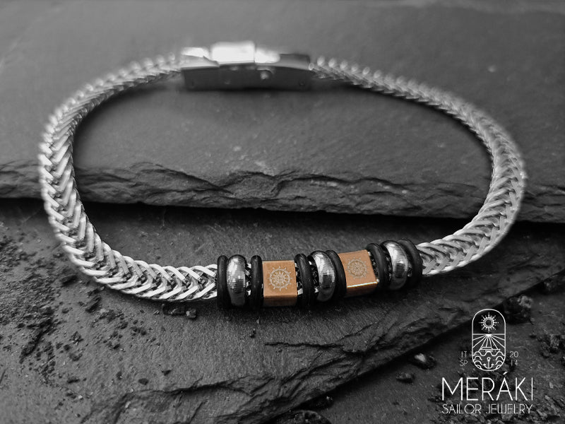 Bracciale realizzato con maglia snake piatta e charm centrali con incisi due timoni dorati