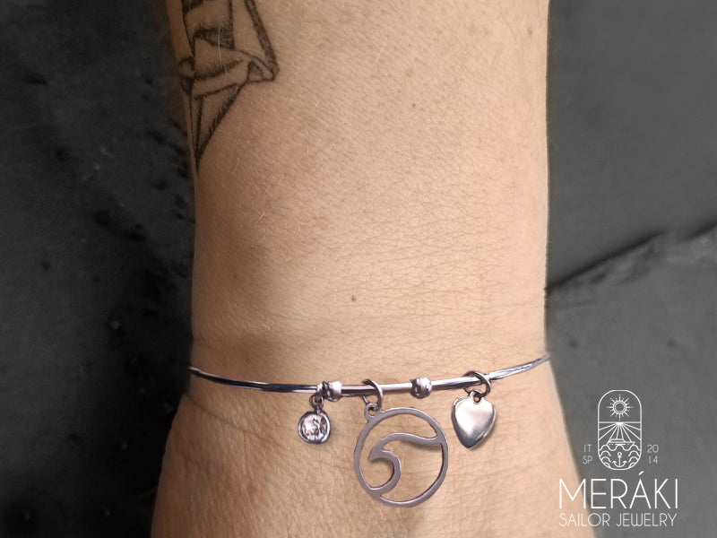 Bracciale rigido Bangle in acciaio con ciondolo dal design ad onda del mare, punto luce e piccolo cuore in acciaio.  Chiusura del bracciale tonda.