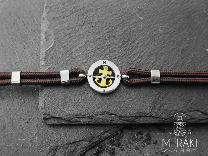 Meraki sailor jewelry bracciale cordino nautico marrone con charm centrale rosa dei venti argentato e ancora girevole dorata