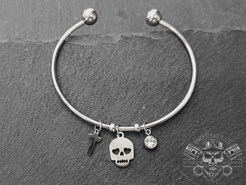 Bracciale rigido Bangle piercing in acciaio con ciondoli dal design a teschio, punto luce e piccola croce in acciaio.