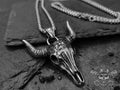 Collana con pendente dal design a teschio di bufalo Texano in acciaio argentato con una patina ossidata che accentua i dettagli e le trame.  Il ciondolo è molto dettagliato sia frontalmente che lateralmente ed è a completamento di una catenina maschile in acciaio con maglia box.