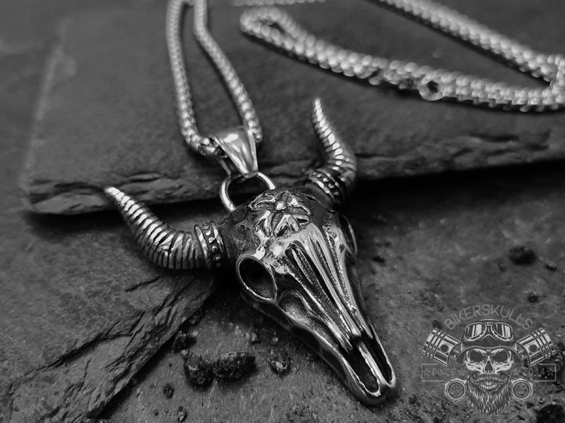 Collana con pendente dal design a teschio di bufalo Texano in acciaio argentato con una patina ossidata che accentua i dettagli e le trame.  Il ciondolo è molto dettagliato sia frontalmente che lateralmente ed è a completamento di una catenina maschile in acciaio con maglia box.