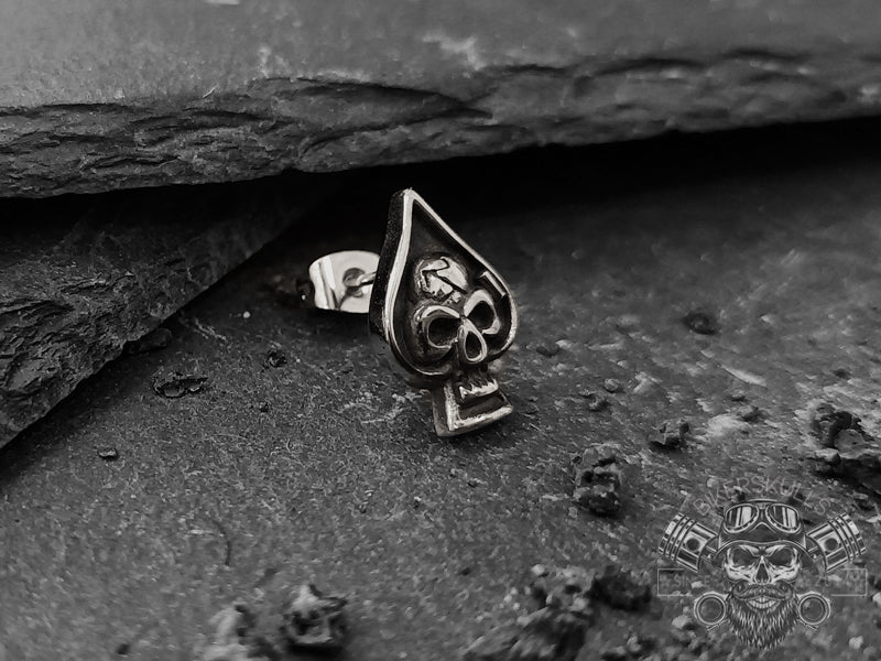 Questo orecchino ha un design aggressivo basato sul poker. Un teschio argentato si staglia su uno sfondo nero a forma di asso di picche.