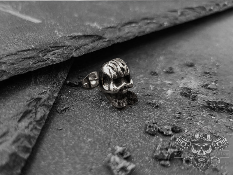 orecchino caratterizzato da un teschio infuocato dettagliatamente rifinito. Gli intensi accenti neri risaltano benissimo sulla superficie in acciaio lucido. 