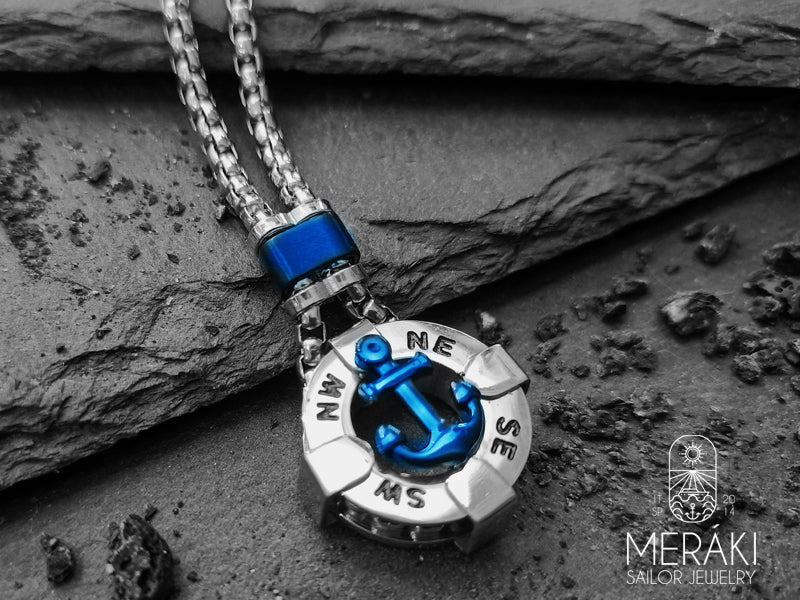 Collana in acciaio inossidabile lucidato, dal design insolito. Il pendente a cappio è a forma di ancora blu, al di sotto della quale figurano i punti cardinali che rendono ancor più maschile questa collana.