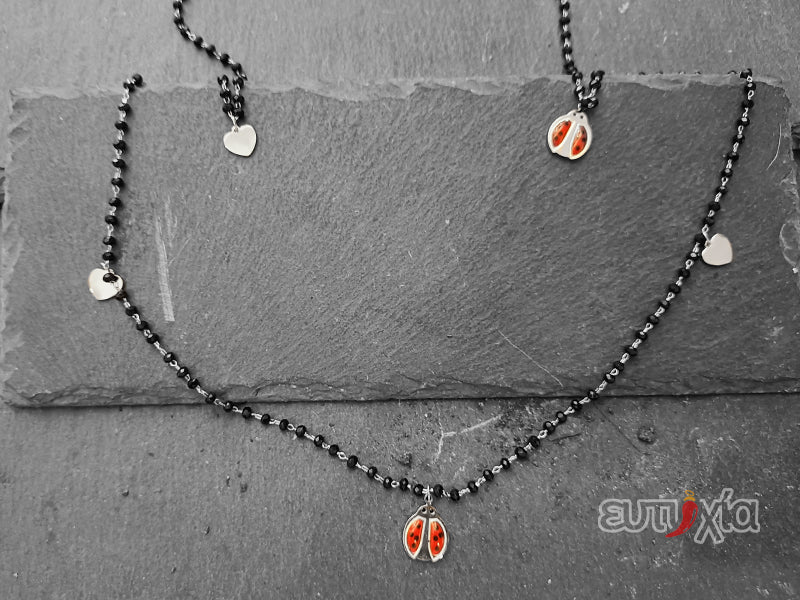 Collana lunga in acciaio 316L cristalli neri con pendenti a forma di coccinella e cuori.