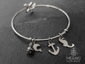 Bangle in acciaio con ciondoli marinari raffiguranti un ancora, un delfino e un cavalluccio marino con una piccola perlina in ceramica e chiusura a stella marina