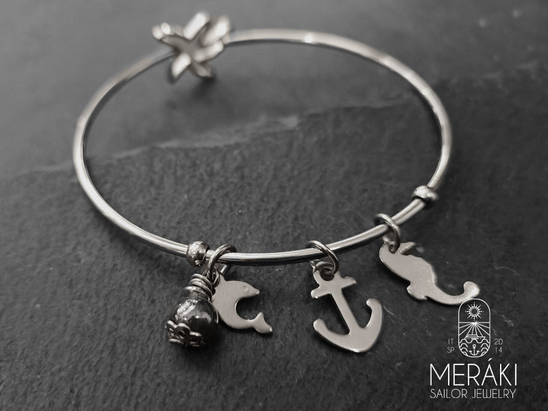 Bangle in acciaio con ciondoli marinari raffiguranti un ancora, un delfino e un cavalluccio marino con una piccola perlina in ceramica e chiusura a stella marina