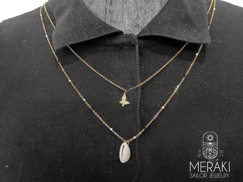 Collana dal design marinaro realizzata in acciaio chirurgico dorato su due file, una girocollo con una farfalla pendente e una seconda con alternate delle perline colorate e una conchiglia Cowrie