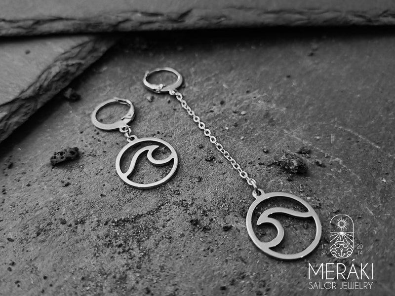 Orecchini a cerchietto con catenella asimmetrici in acciaio chirurgico la cui caratteristica distintiva è il design a forma di onda.