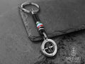 Portachiavi Kai realizzato con cordino nautico nero, charm centrale con bandiera Italiana. A completamento del portachiavi troviamo un charm con ancora girevole nera, rosa dei venti con i punti cardinali a contrasto